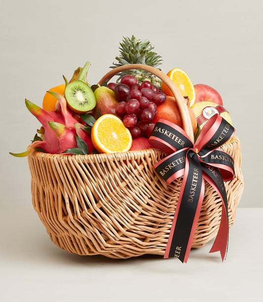 Wicker fruit hamper with fresh grapes, oranges, kiwi, pear, dragon fruit, and pineapple