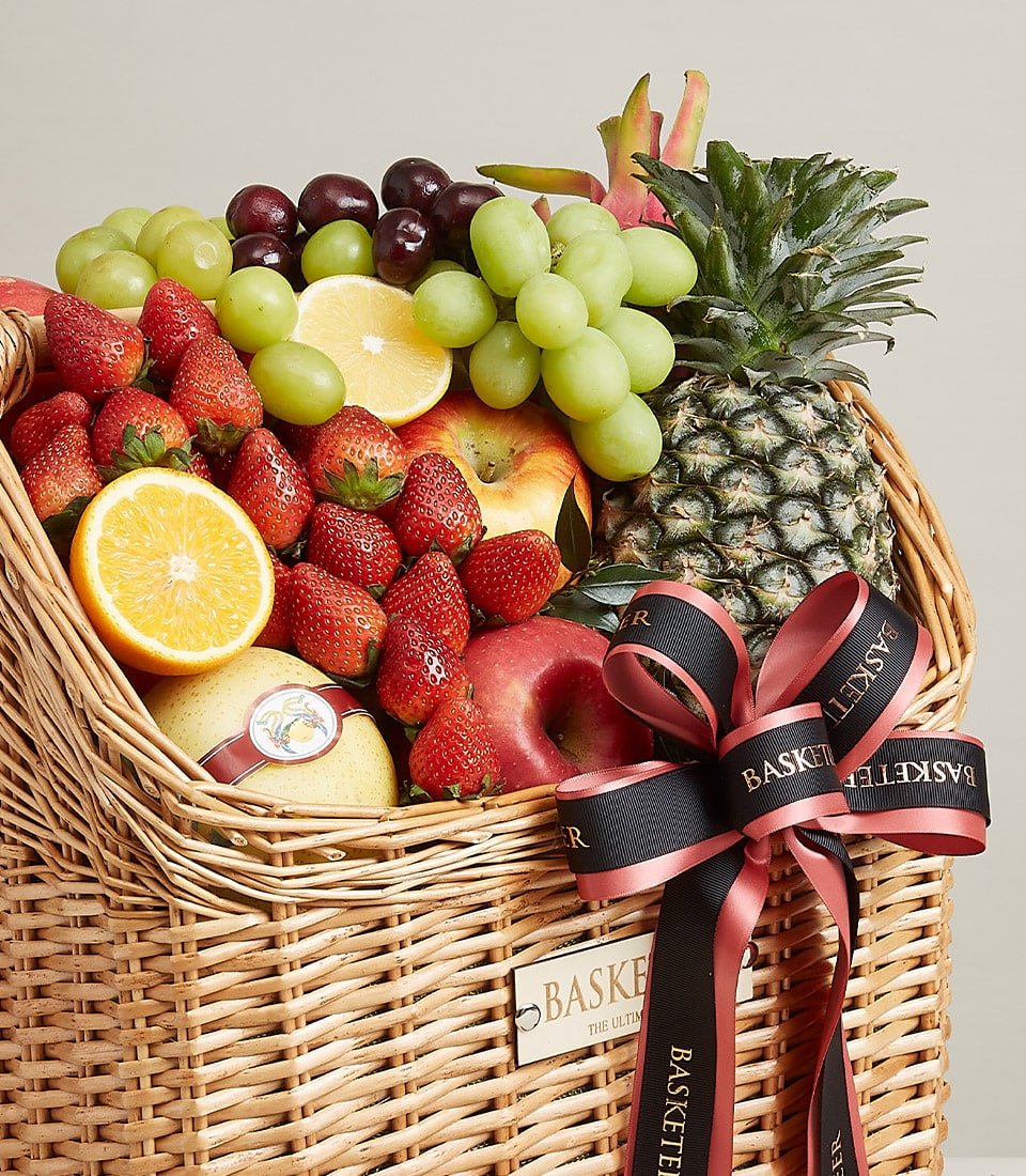 Luxury fruit gift basket with fresh grapes, strawberries, pineapple, apples, pears, and citrus in wicker with black ribbon