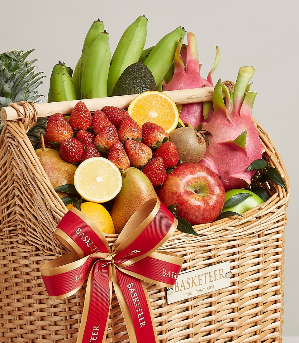 Opulent wicker fruit basket with fresh bananas, avocado, dragon fruit, pineapple, strawberries, citrus, apples and pears,