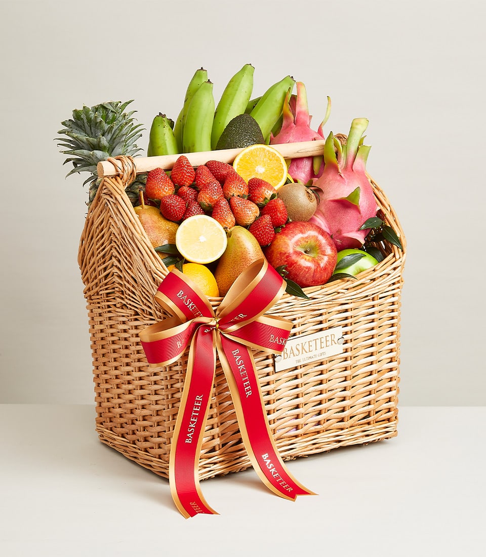Premium wicker fruit basket with fresh apples, strawberries, dragon fruit, and tropical selection tied with red ribbon