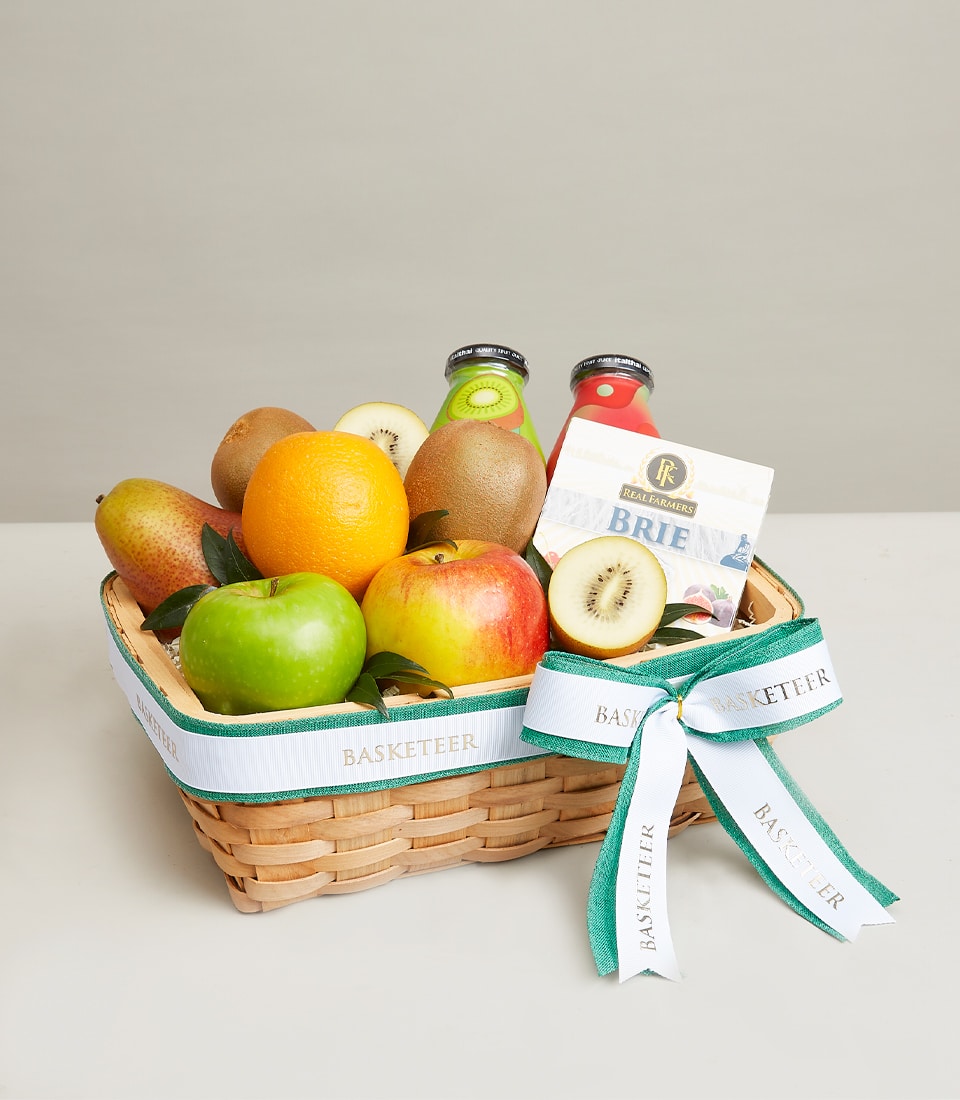 Woven wicker basket filled with fresh apples, pears, oranges, kiwis, gourmet brie cheese, and artisan juices with green