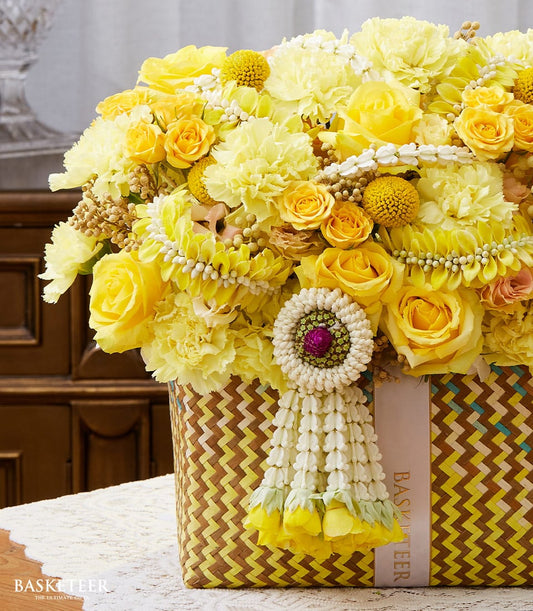 Vibrant yellow roses and carnations in woven basket with Thai phuang malai garland for Songkran celebration
