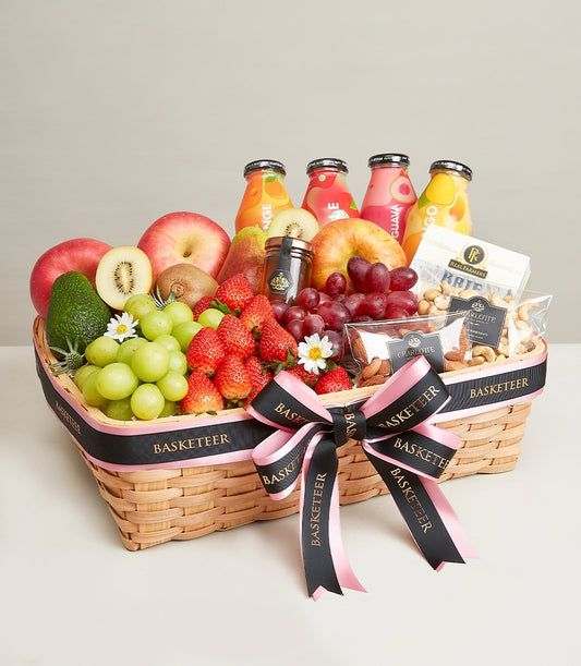 Woven wicker gift basket with fresh fruits, gourmet juices, nuts, and honey jars tied with black and pink ribbon
