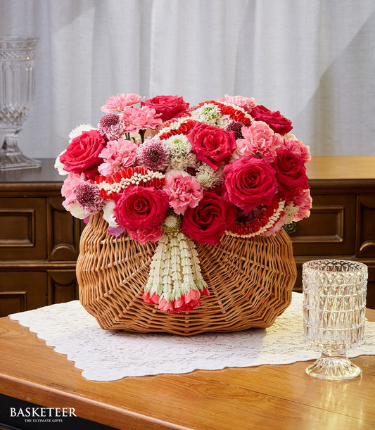 Vibrant red and pink rose arrangement in woven basket with white floral garland for New Year celebrations by Flowers by