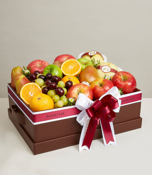Premium luxury fruit gift box with red apples, pears, grapes, and oranges in brown leather hamper with maroon ribbon bow