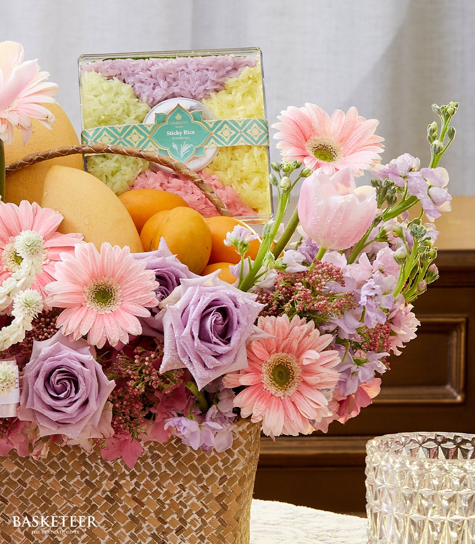 Woven rattan gift basket with fresh flowers, tropical fruits, and colorful sticky rice for Songkran celebration