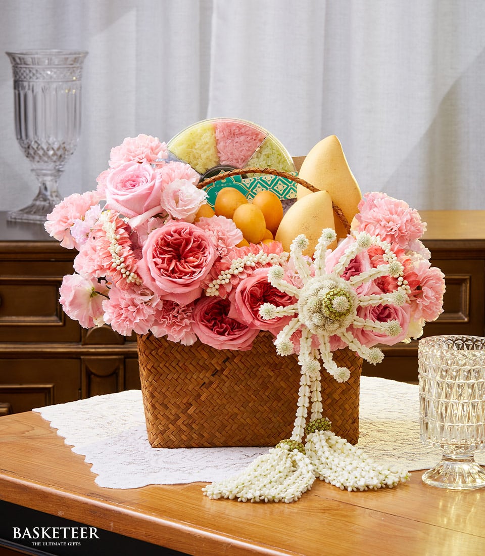 Woven basket brimming with pink roses, carnations, fresh mangoes, and tropical fruits with sticky rice selection for Thai