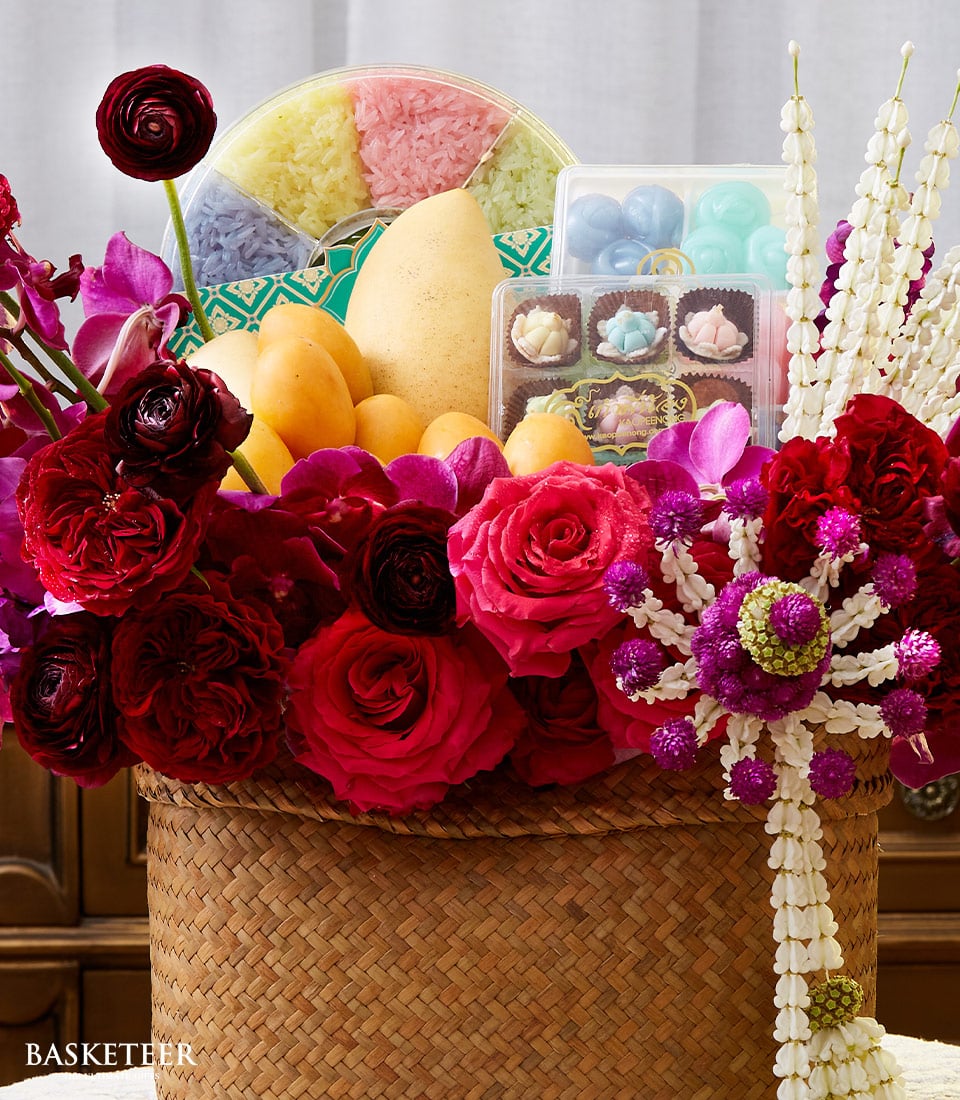 Vibrant gift basket with fresh mangoes, red roses, orchids, colorful sticky rice, Thai desserts, and jasmine garland for