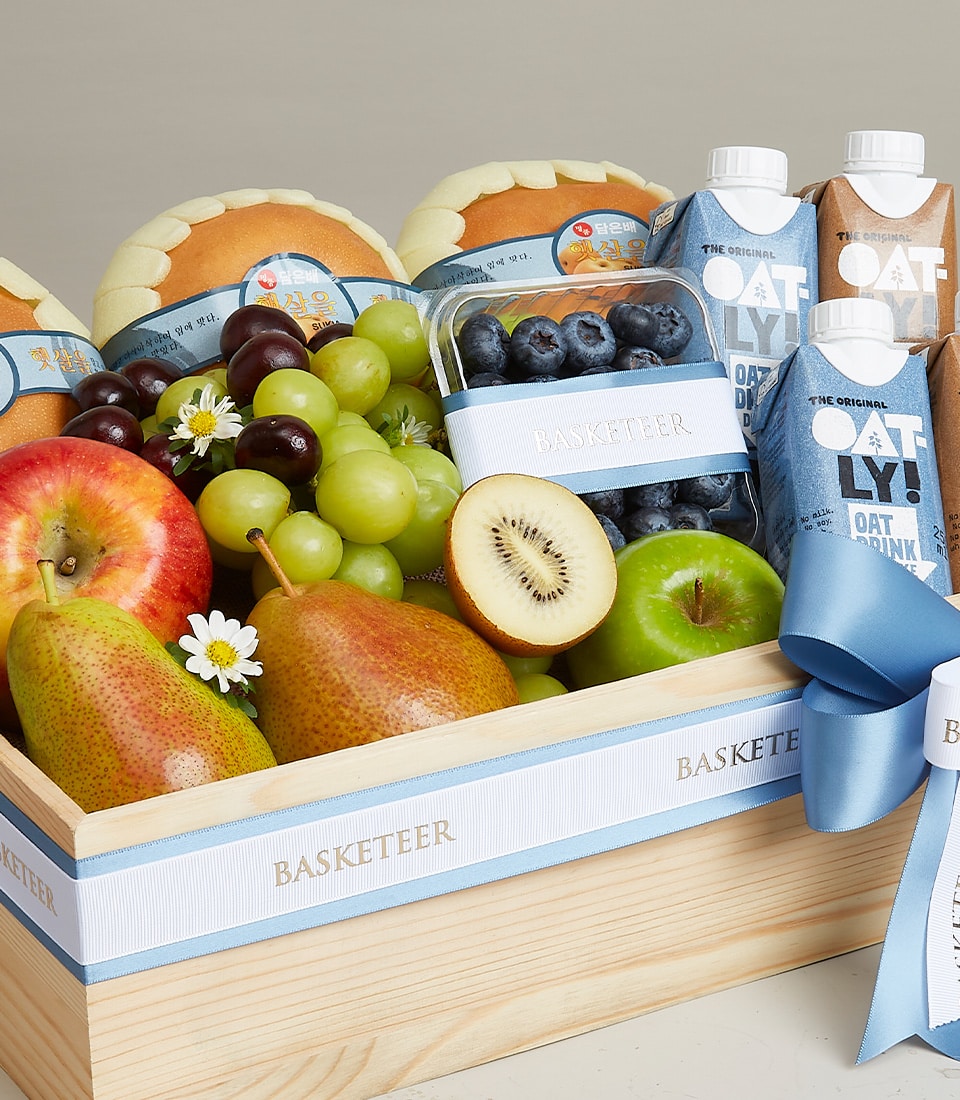 Wooden gift crate with fresh grapes, apple, pears, kiwi, blueberries, oat milk cartons and artisan bread rolls tied with