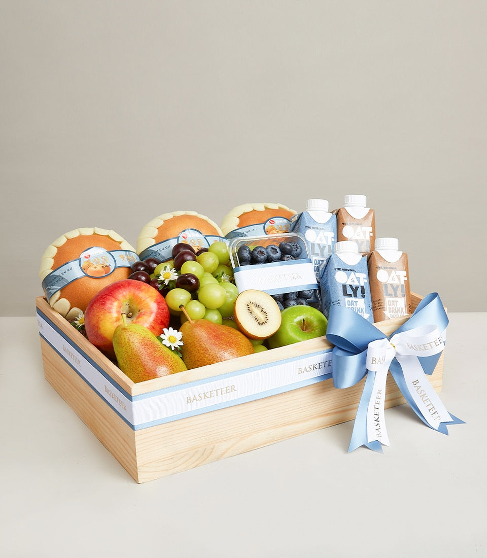 Wooden gift box with fresh citrus, grapes, berries, and Oatly oat drink wellness basket