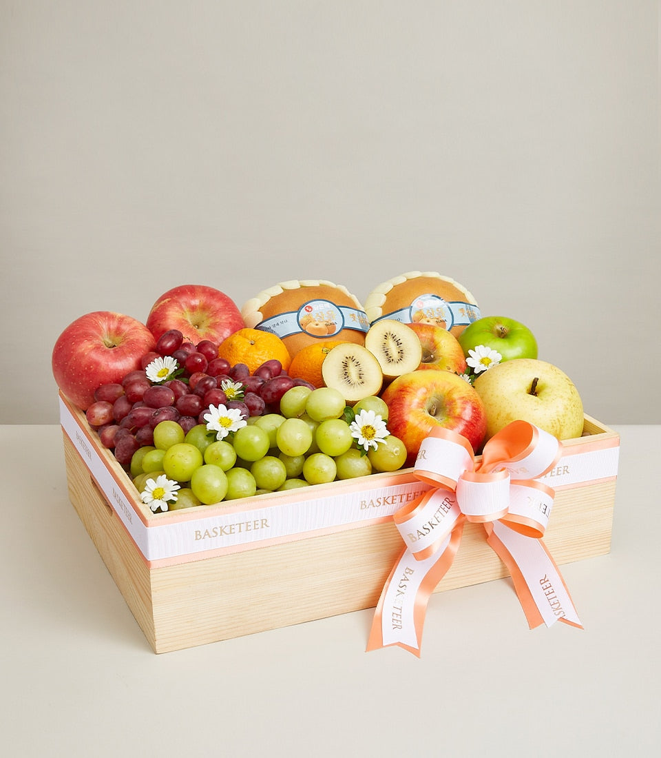 Deluxe fresh fruit box with apples, grapes, oranges, kiwi and pear in wooden basket with white ribbon