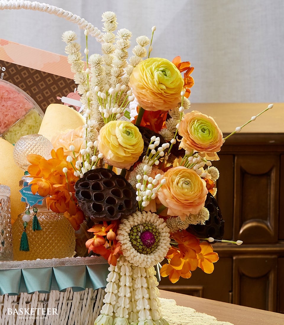 Yellow and orange ranunculus Songkran gift basket with white wicker, jasmine garland, and artisan treats