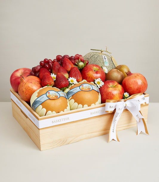 Light wooden gift box brimming with fresh apples, pears, pomegranates, grapes, strawberries, and kiwis, tied with white