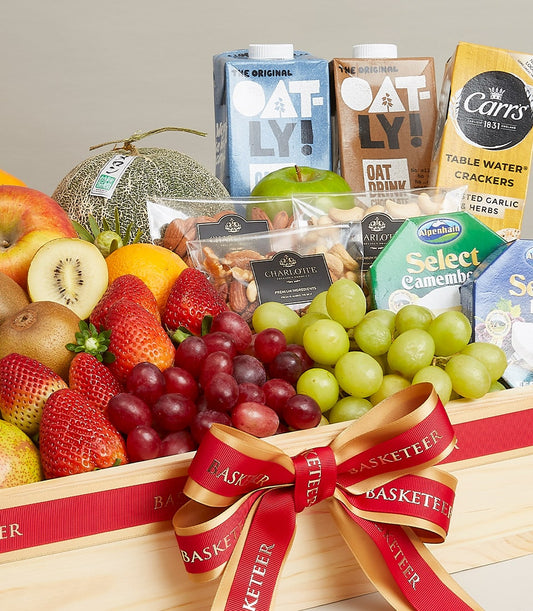 Wooden gift basket with fresh fruits, artisan cheeses, nuts, and gourmet crackers tied with red ribbon