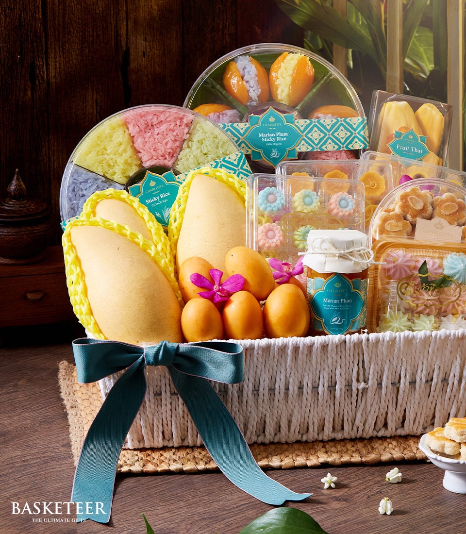 Woven white gift basket with fresh Thai mangoes, Marian plums, orchids, and assorted sticky rice sweets for Songkran