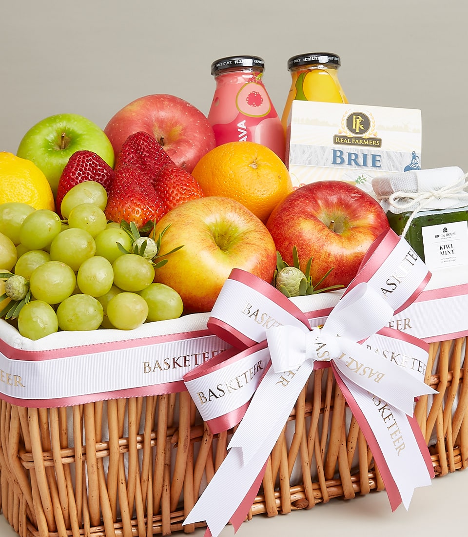 Woven wicker gift basket with fresh fruits, Brie cheese, and gourmet preserves tied with white ribbon