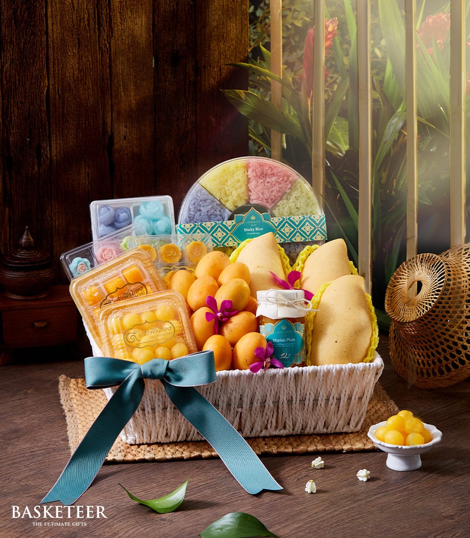 Woven white gift basket with teal ribbon filled with Thai sticky rice, traditional sweets, mangoes, and Marian plums for