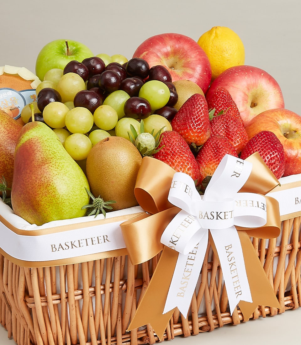 Premium mixed fresh fruit basket in woven wicker with green and red apples, grapes, kiwis, strawberries, pears and lemons