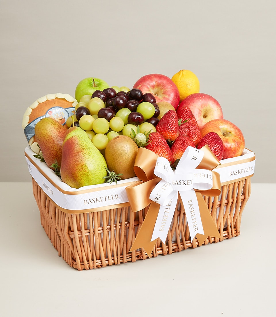 Woven wicker basket filled with fresh mixed fruits, apples, pears, grapes, and berries tied with white ribbon