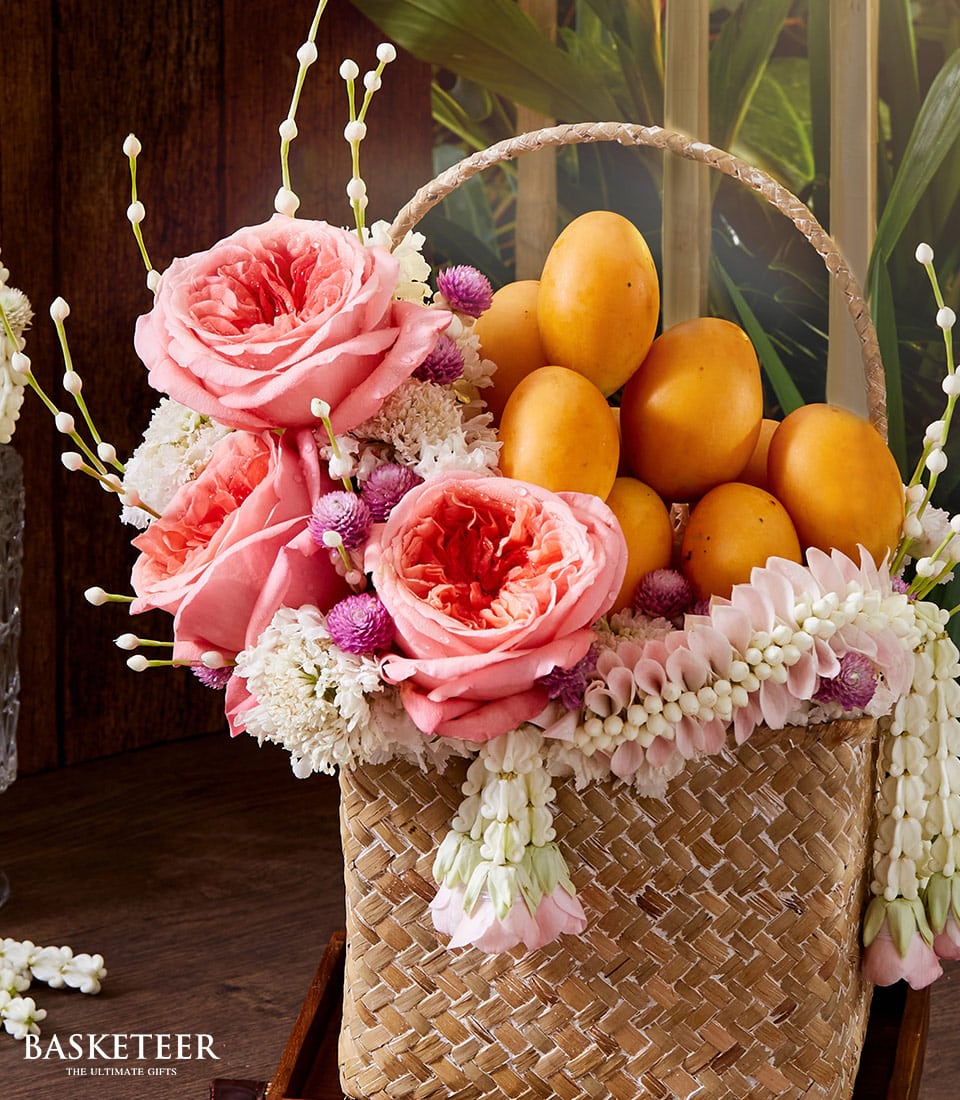 Woven rattan gift basket with pink roses, purple filler flowers, and Thai marian plums for Thai New Year