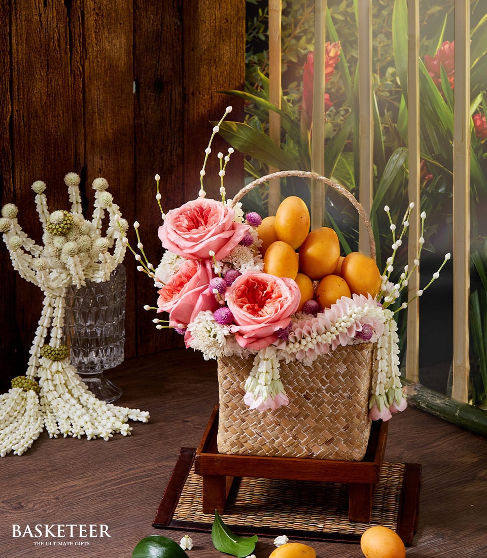 Woven straw gift basket with pink roses, white flowers, and Thai marian plums for Songkran New Year