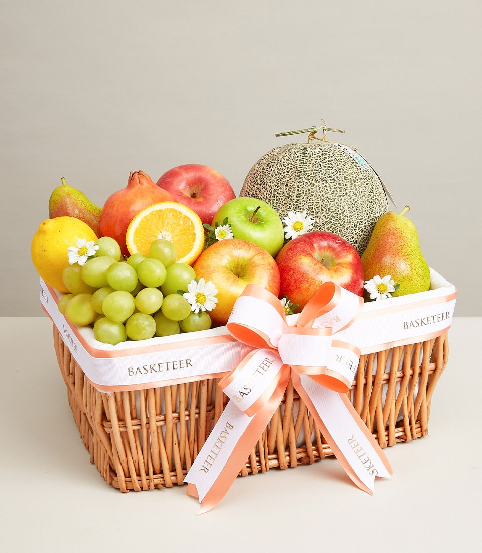 Woven wicker fruit basket with fresh apples, grapes, lemons, pears, melon and pomegranate, tied with white ribbon bow
