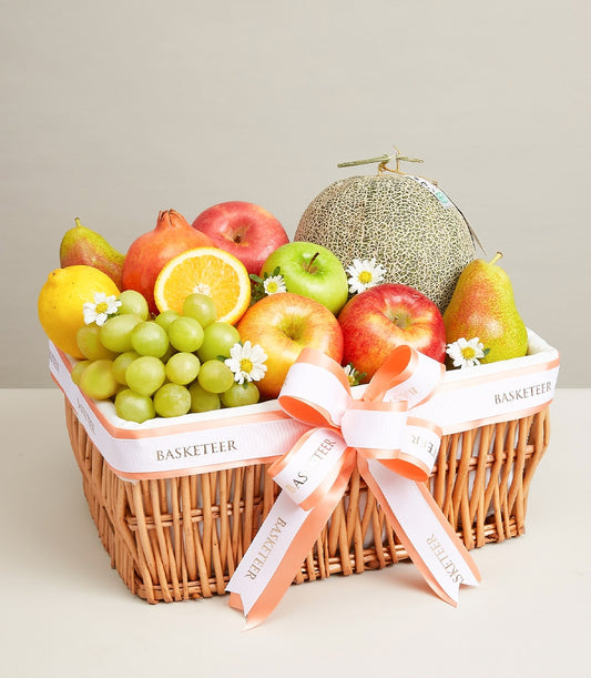 Woven wicker fruit basket with fresh apples, grapes, lemons, pears, melon and pomegranate, tied with white ribbon bow