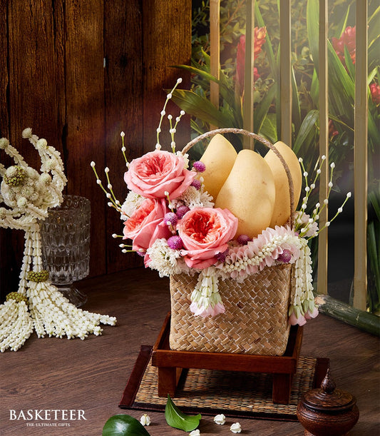 Woven basket with fresh pink roses, white blooms, purple flowers, and ripe yellow mangoes for Thai New Year