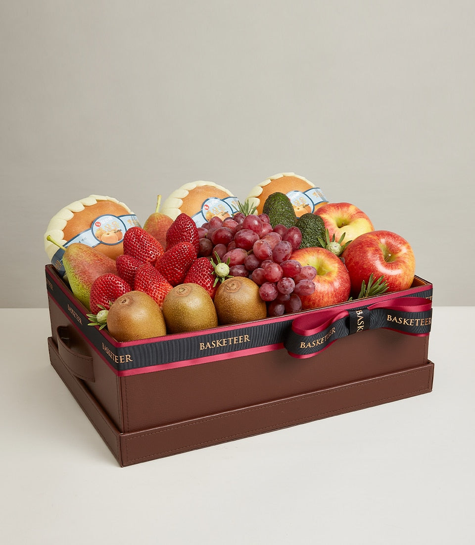 Luxury fruit gift box with red apples, pears, strawberries, grapes, and kiwis in brown leather container with black ribbon