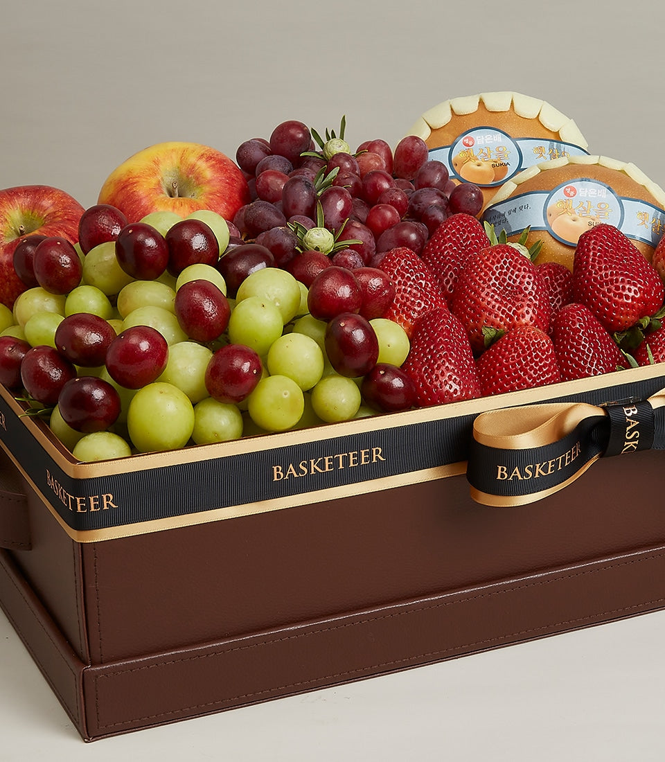 Luxury fruit gift box with fresh grapes, apples, strawberries, and pears in dark brown leather-like packaging with black and