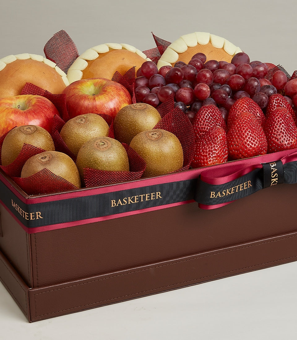 Luxury brown leather gift box filled with fresh kiwis, red apples, grapes, strawberries, and pears with black ribbon