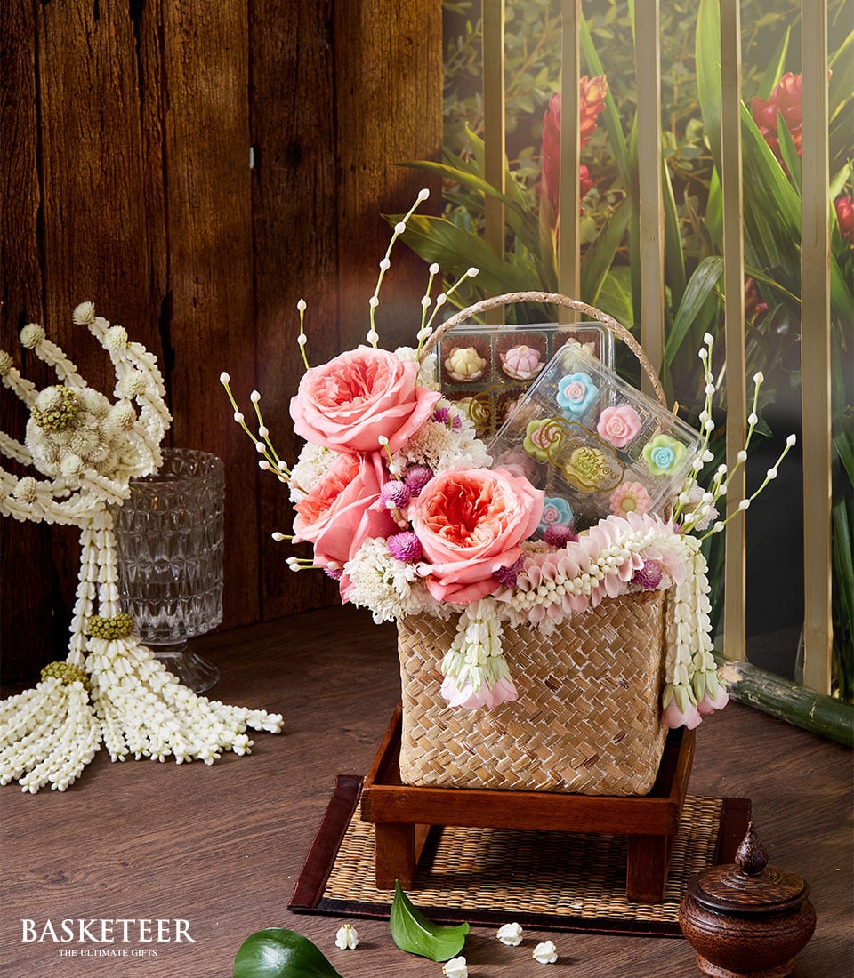 Woven straw gift basket with pink roses, white and purple flowers, and flower-shaped confections for Thai New Year