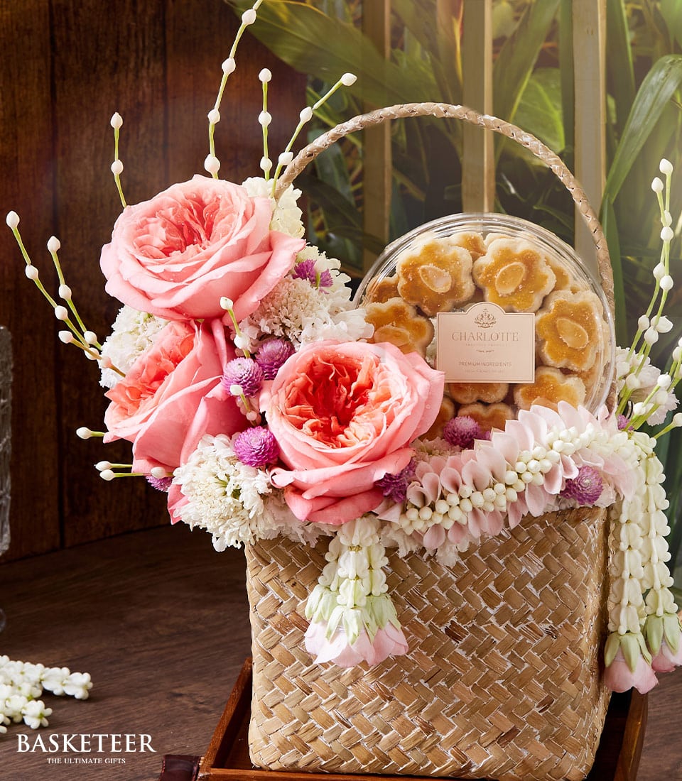 Woven straw gift basket with pink roses, white flowers, and almond cookies for Thai New Year