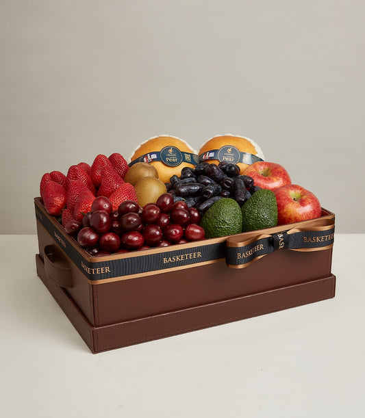 Luxury gourmet fruit gift box with strawberries, cherries, grapes, pears, and avocados in dark brown leather case with