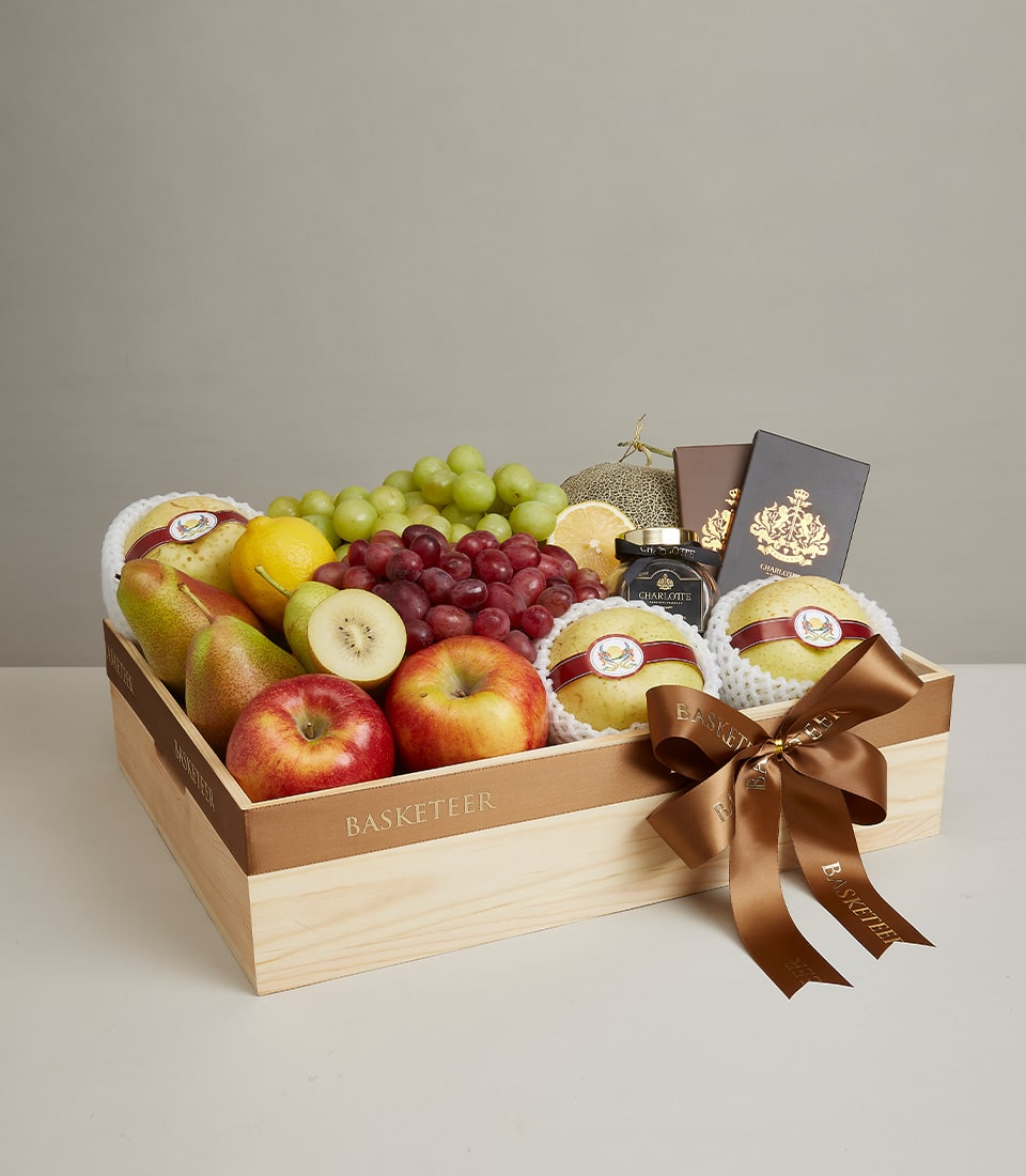 Wooden gift box filled with fresh grapes, apples, pears, kiwi, lemon, cantaloupe, and gourmet items with gold-trimmed satin