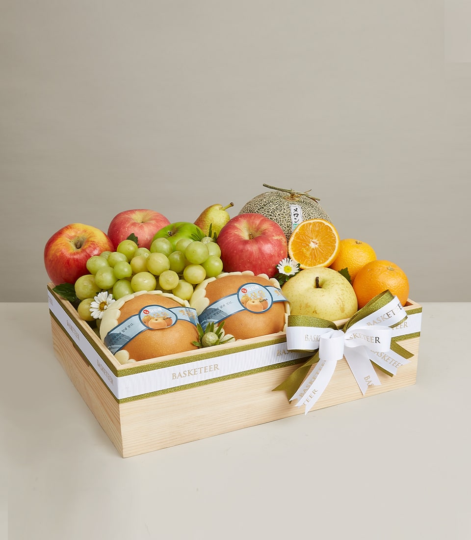 Wooden gift box with assorted fresh fruits, red and green apples, grapes, oranges, and Asian pears, white ribbon bow