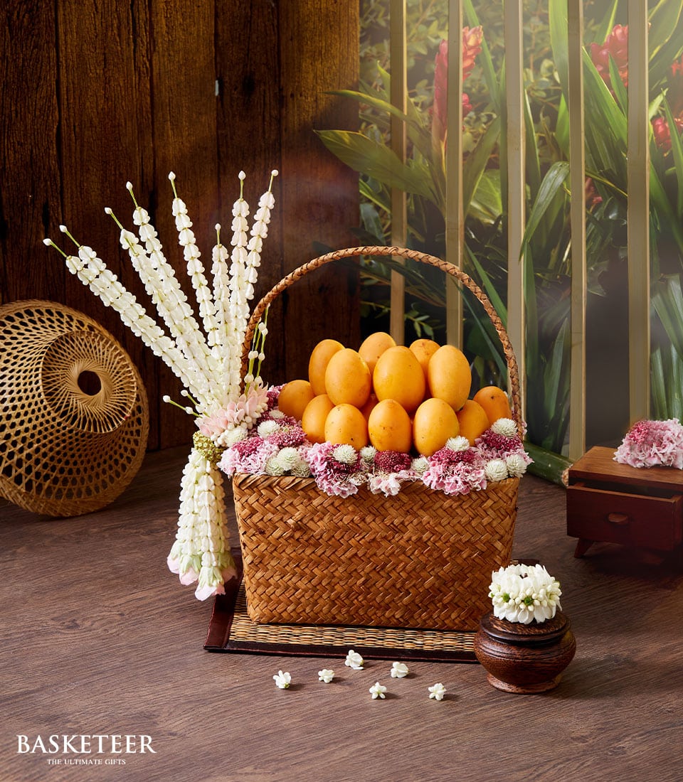 Woven basket of golden Thai mangoes with white and pink flower garland for Songkran celebration