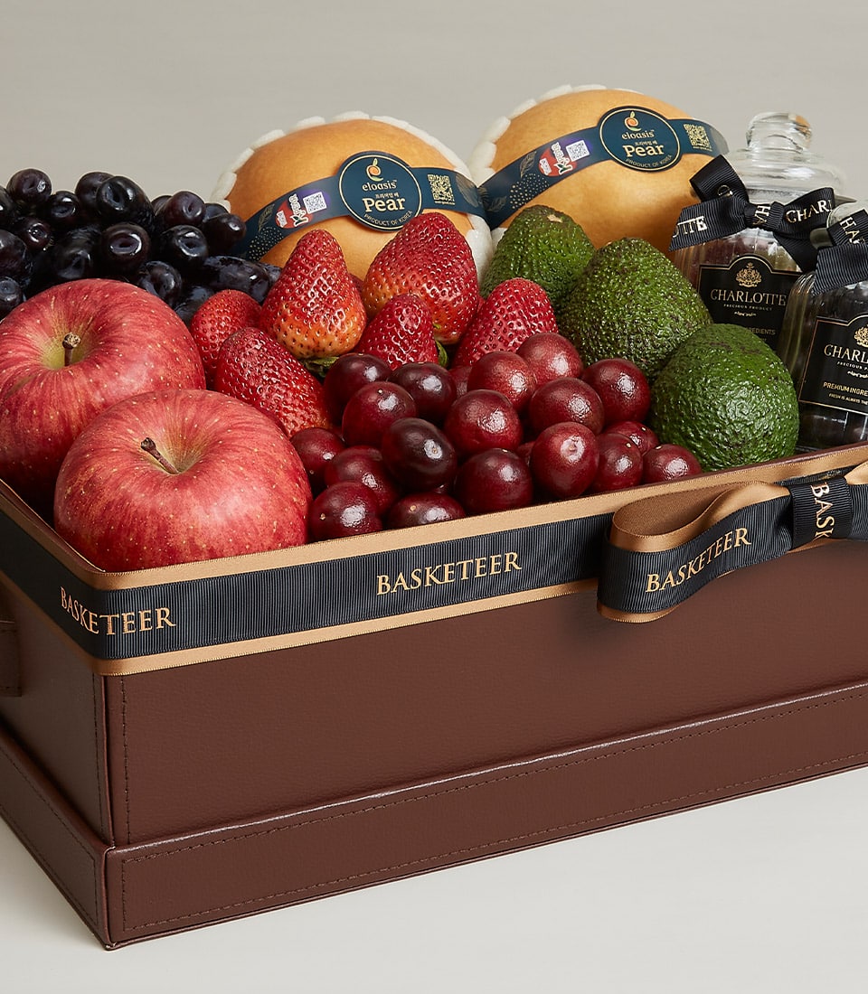 Luxury fruit gift basket with fresh apples, grapes, strawberries, cherries, pears, avocados and gourmet items in dark