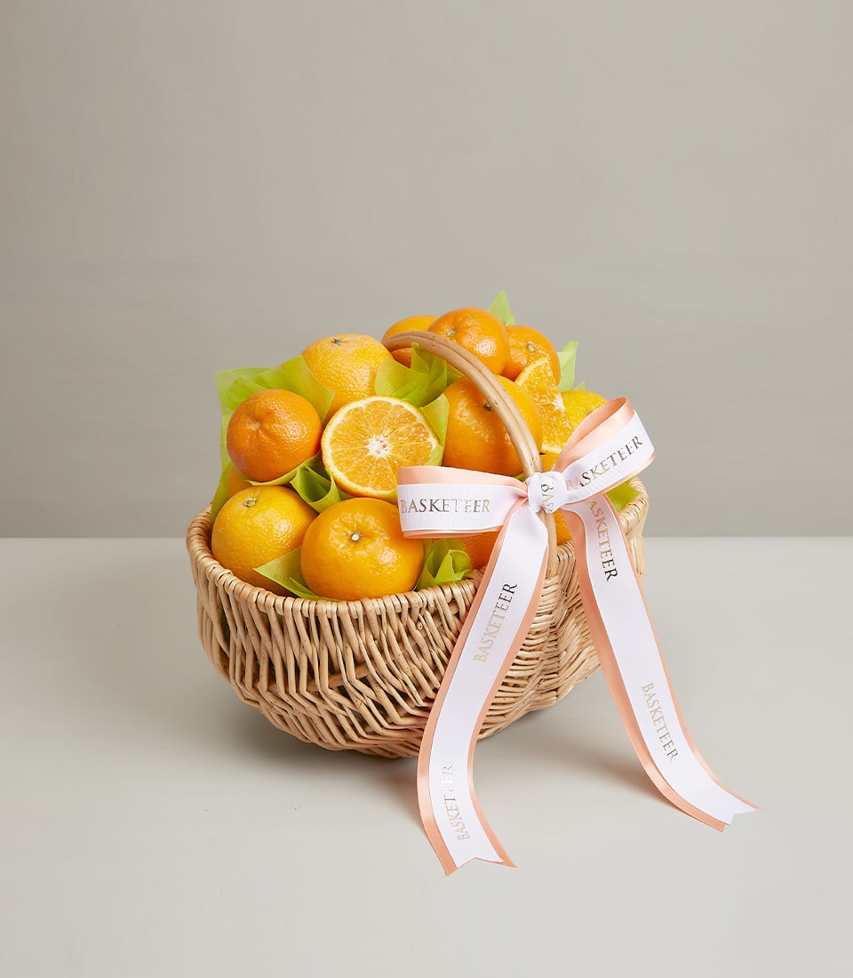 Premium wicker basket filled with fresh oranges and green tissue, tied with gold-trimmed ribbon