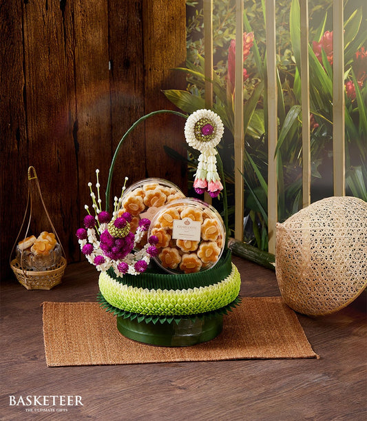 Flower-shaped almond cookies in stacked containers with banana leaf base, purple amaranth, and Thai floral garland for