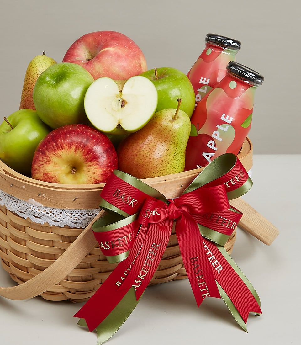 Woven fruit gift basket with fresh apples, pears, and apple juice bottles tied with festive red ribbon