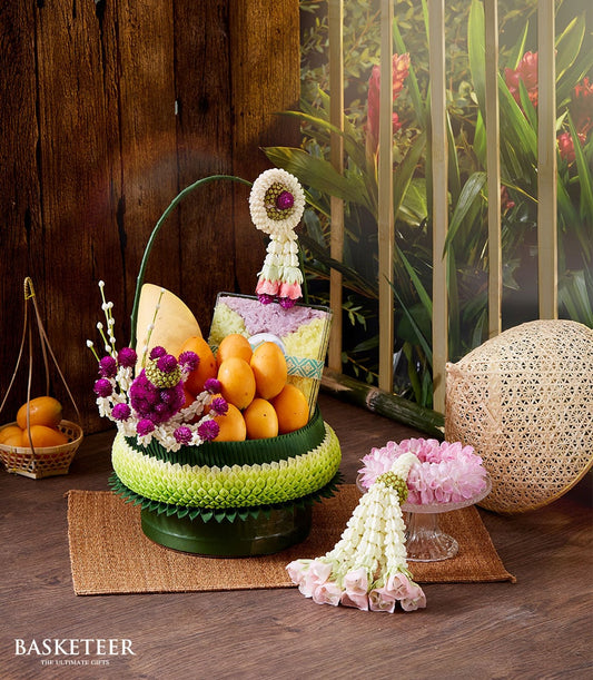 Thai mango and tropical fruit gift basket with layered sticky rice, purple amaranth flowers, and woven green tiers for