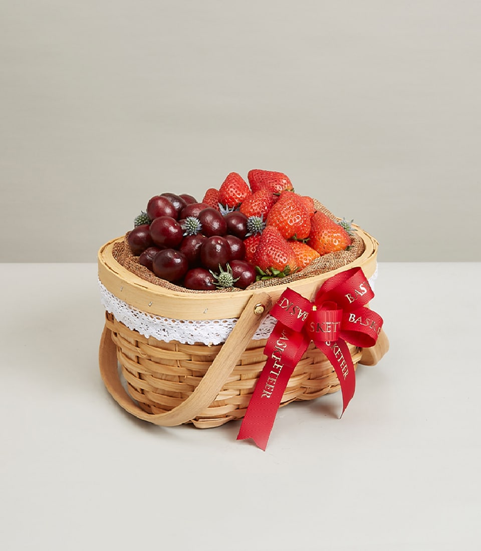 Woven wicker fruit basket with fresh strawberries, cherries, and blue thistles, tied with red ribbon for birthdays