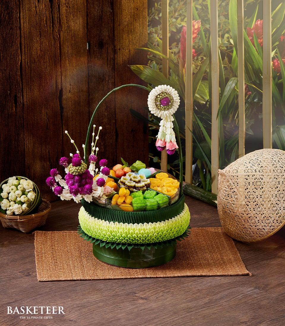 Tiered dark green Thai gift basket with traditional sweets, phuang malai garland, and fresh flowers for Songkran celebration