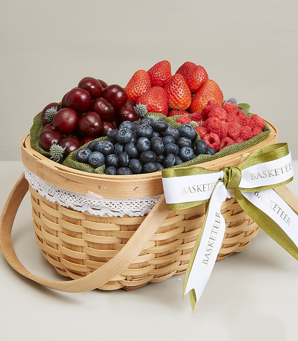 Luxury woven berry fruit basket with fresh cherries, strawberries, blueberries, and raspberries, white lace trim, and gold