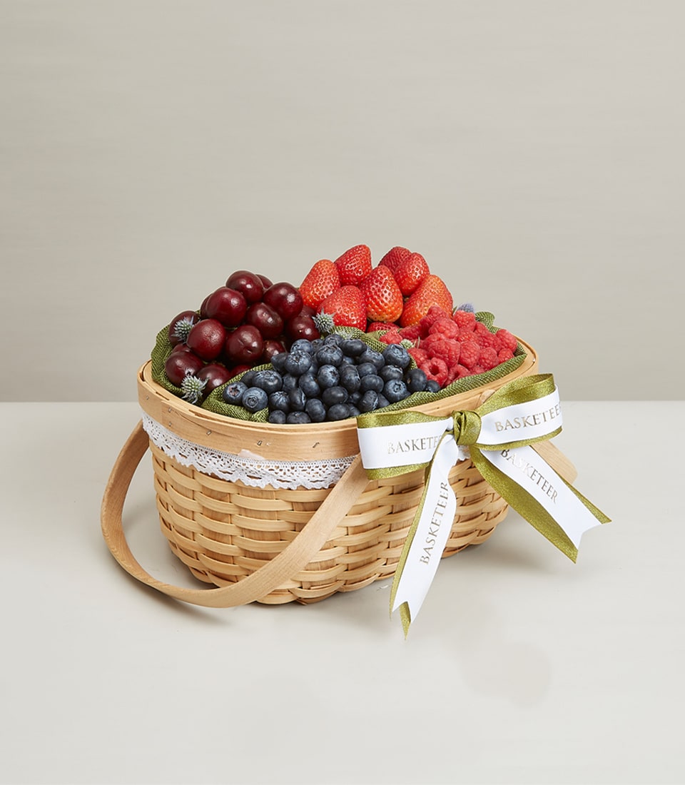 Luxury woven basket brimming with fresh cherries, strawberries, blueberries, and raspberries on green fabric liner