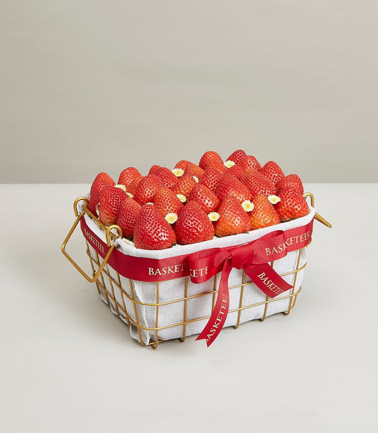 Luxury gold wire basket filled with fresh red strawberries, white flowers, and red ribbon bow for premium gifting