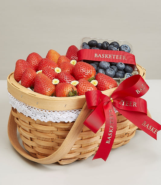 Woven wicker fruit basket with fresh strawberries and blueberries, red ribbon bow, birthday gift