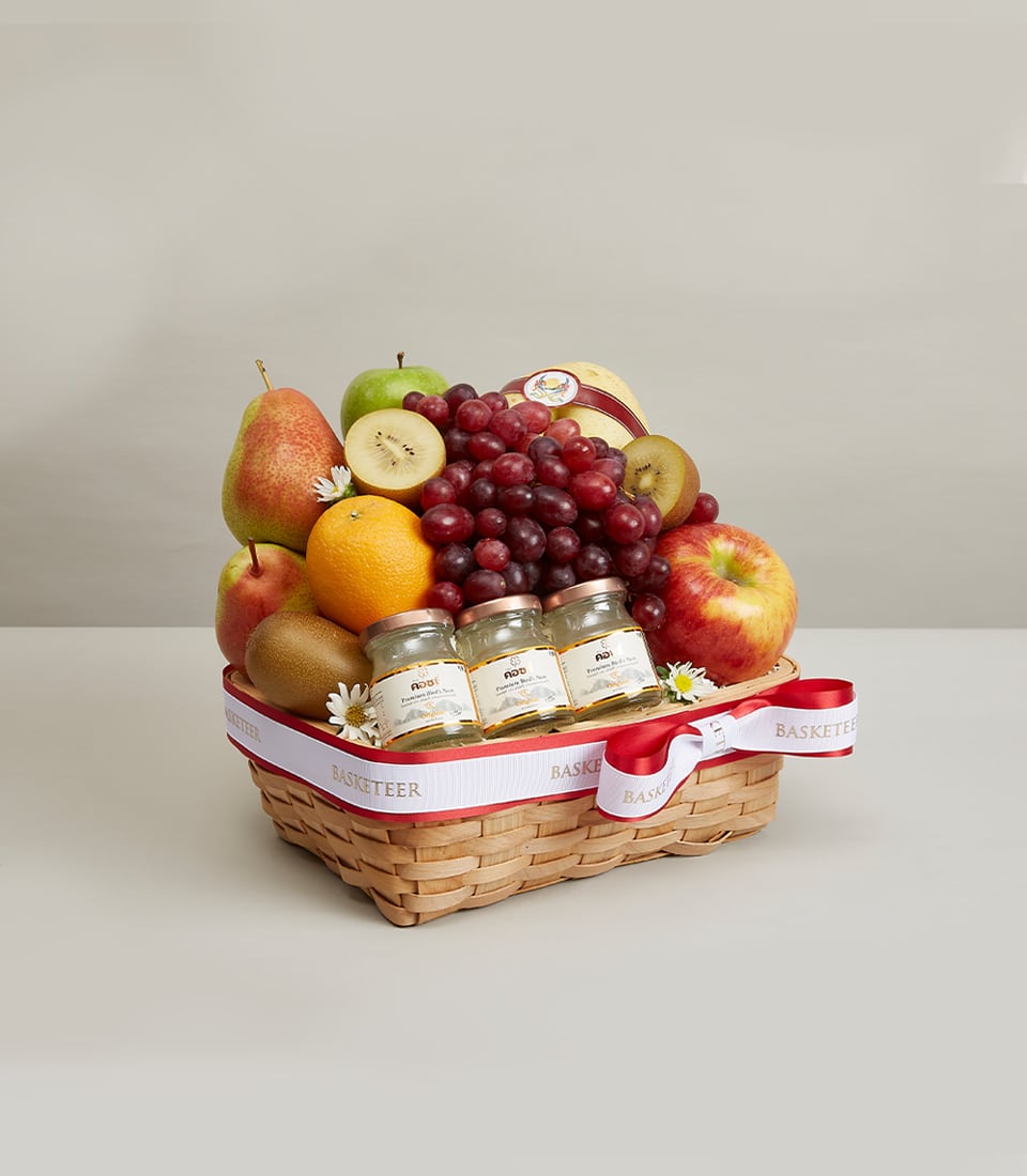 Premium fruit basket with red grapes, pears, oranges, kiwi, and artisan treats in woven light brown basket with white ribbon