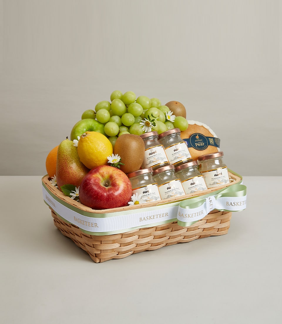 Woven wicker fruit basket with fresh grapes, apples, pears, citrus, and premium bird's nest jars with rose gold lids